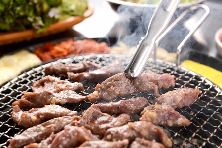 Tongs grabbing pork skirtmeat, being grilled, on a grill placed over charcoalの写真素材
