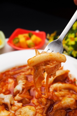 Fork lifting tteokboki, a Korean cuisine, rice cake and fish cakes stir-fried with spicy sauce, on a white plateの写真素材