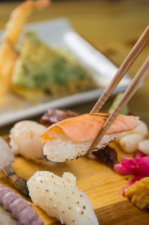 Chopsticks grabbing grilled salmon sushi among assorted sushi, on a wooden cutting boardの写真素材