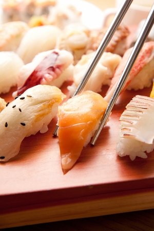 Chopsticks grabbing salmon sushi among assorted sushi, on a wooden cutting boardの写真素材