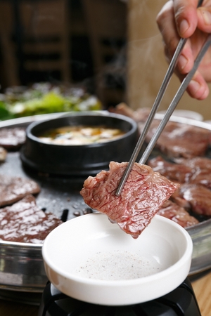 Chopsticks grabbing grilled beef, dipping in saltの写真素材