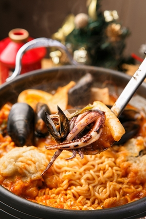 Spoon lifting seafood tteokboki, a Korean cuisine, rice cake, fish cakes, and seafood stir-fried with spicy sauce, boiling in a black potの写真素材