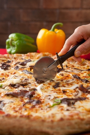 Pizza cutter cutting a barbecued beef pizza with onions, barbecued beef, cheese and paprika, on thin doughの写真素材