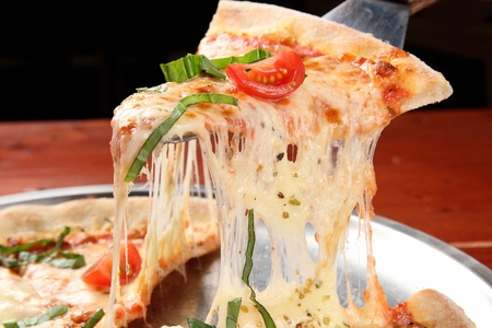 Cheese pizza with cherry tomatoes and parsley, picked up by a pizza serverの写真素材