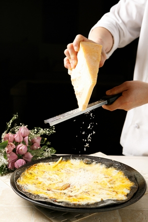 Chef's hand sprinkling cheese on potato pizza made of black doughの写真素材