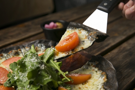 Pizza server picking up salad pizza with tomatoes and vegetables, made of black doughの写真素材