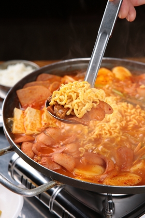 Ladle picking up Korean-style kimchi stew with various sausages (Budae-jjige)
