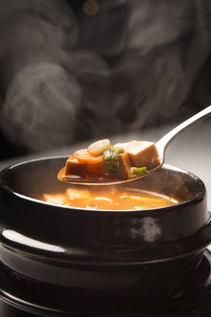 Spoon picking up Korean-style bean-paste stew (Dwenjang-jjige), cooked with bean-paste, various vegetables and tofuの写真素材