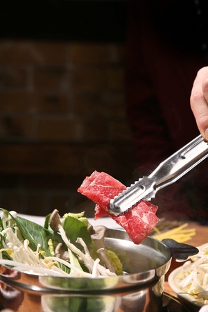 Thin beef going in a hotpot with boiling vegetables