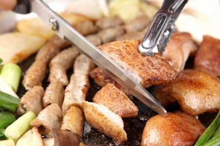 Scissors cutting pork entrails on black grillの写真素材