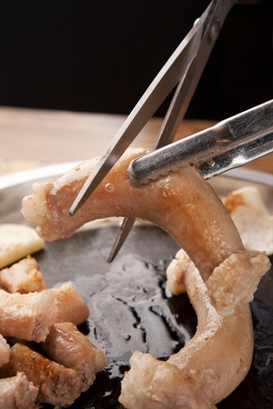 Scissors cutting pork tripes, on grillの写真素材