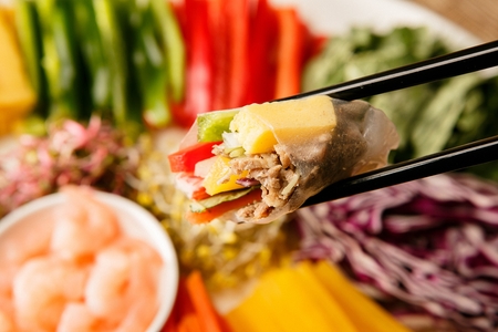 Chopsticks picking up Vietnamese spring rolls, made of rice paper, vegetables, shrimps etc.