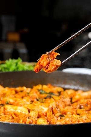 Chopsticks picking up spicy stir-fried chicken, cooked with various vegetables, on black fire grillの写真素材