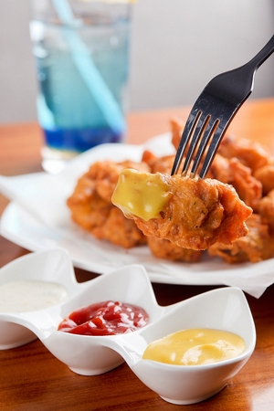 Boneless fried chicken being dipped in mustard sauceの写真素材