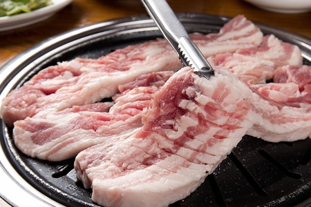 Pincers turning pork belly with cuts on black grillの写真素材