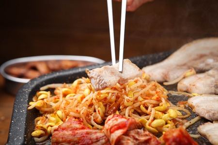 Chopsticks picking up pork belly being grilled on black grillの写真素材