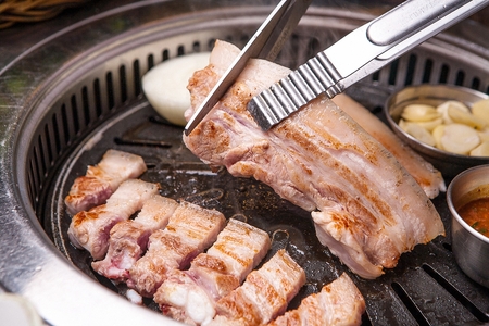 Scissors cutting pork belly on black grillの写真素材