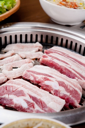 Pork belly with cuts and pork cheek meat being grilled on grillの写真素材