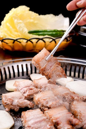 Chopsticks lifting pork belly on black grillの写真素材