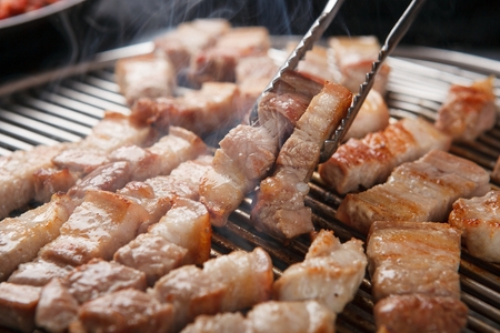 Pincers turning pork skin being grilled on charcoal grillの写真素材