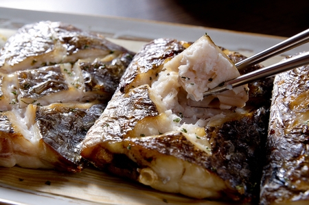 Chopsticks picking up grilled cutlassfish with cuts on white plate