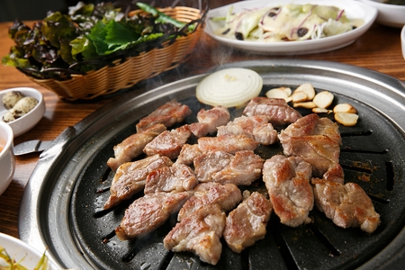 Pork neck, onions, garlic being grilled on black grillの写真素材