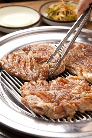 Pincers picking up marinated pork spareribs on grillの写真素材