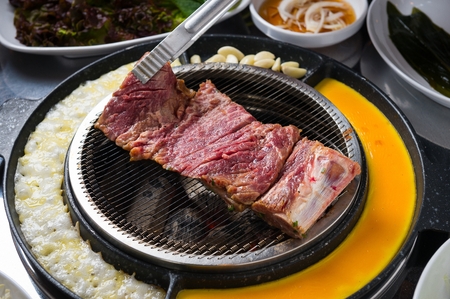 Pincers turning marinated pork spareribs being grilled on charcoal grillの写真素材