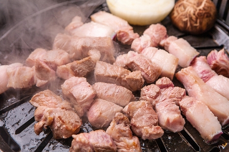 Pork neckm onions, shittake being grilled on black grillの写真素材