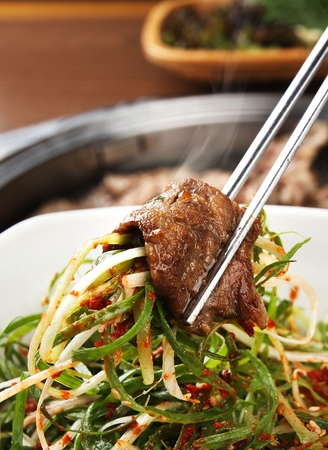 Chopsticks picking up grilled pork belly with seasoned greensの写真素材