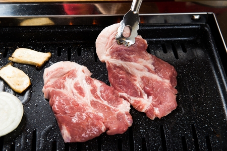 Pincers picking up pork neck being grilled on black grill
