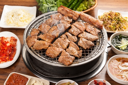 Marinated pork spareribs being grilled on charcoal grill, with side dishesの写真素材