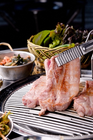 Pincers turning pork belly on charcoal grillの写真素材