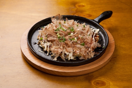 Okonomiyaki, japanese pancakes with dried bonito, mayonnaise, teriyaki sauce, on black oven plateの写真素材