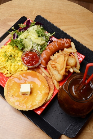 Waffles, scrambled eggs, french fries, sausages, salad on red plateの写真素材