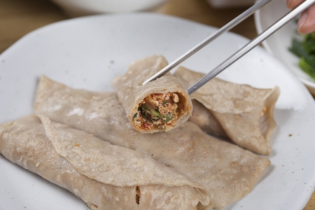 Chopsticks picking up buckwheat crepe, made of glass noodles, tofu and vegetables, on round plate