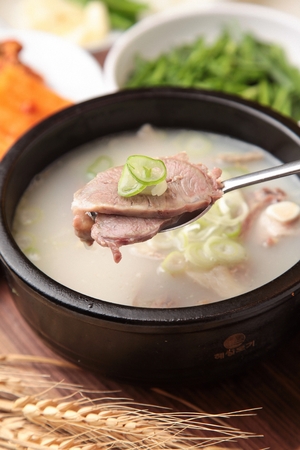 Spoon scooping up korean sausages soup in black potの写真素材