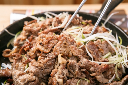 Soy sauce marinated pork and seasoned onions being grilled on black iron plateの写真素材