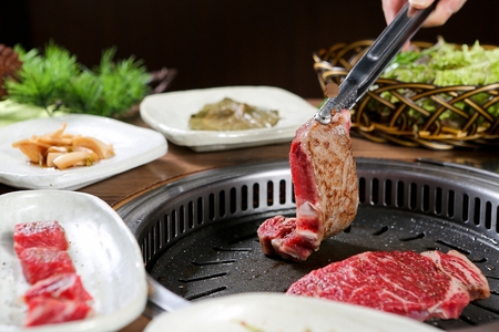 Pincers turning Beef sirloin with sprinkled salt and pepper being grilled on black grillの写真素材