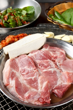 Pork belly, king oyster mushrooms, garlic, kimchi on round silver plateの写真素材