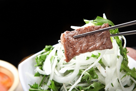 Chopsticks picking up beef sirloin and onion being grilled on charcoal grate