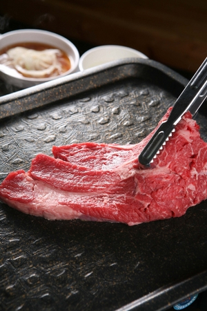 Pincers turning beef sirloin being grilled on black grillの写真素材