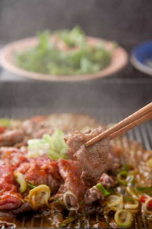 Chopsticks picking up barbecued beef marinated in soy sauce, being grilled on black grillの写真素材