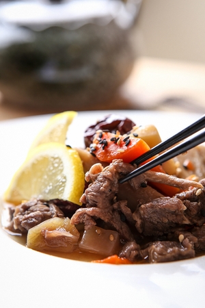Chopsticks picking up thin pork, vegetables marinated in soy sauce, on round plateの写真素材