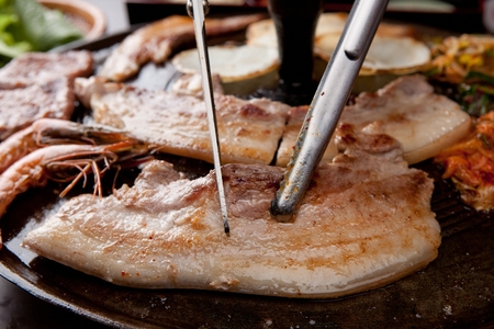 Scissors cutting pork belly being grilled on black grillの写真素材