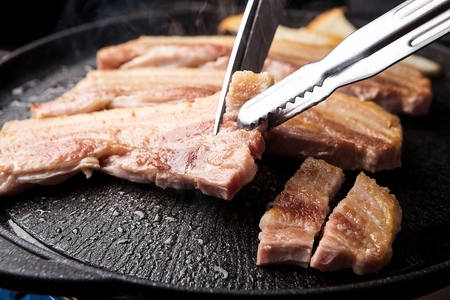 Scissors cutting pork belly being grilled on black grillの写真素材