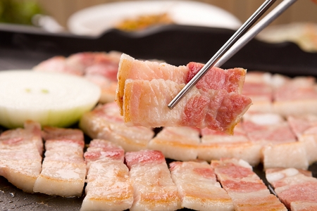 Chopsticks picking up pork belly being grilled on black grillの写真素材