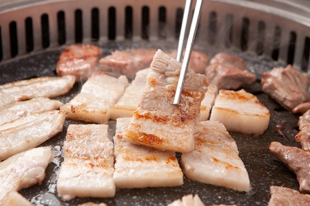 Chopsticks picking up pork belly being grilled on charcoal grillの写真素材
