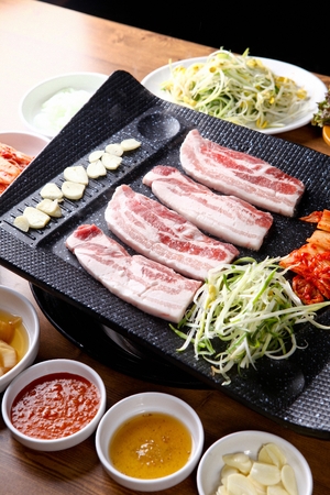 Pork belly, garlic, seasoned green onions, kimchi, being grilled on black grillの写真素材