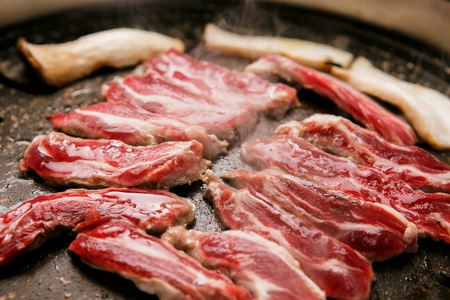 Beef ribs and king oyster mushrooms being grilled on black grillの写真素材